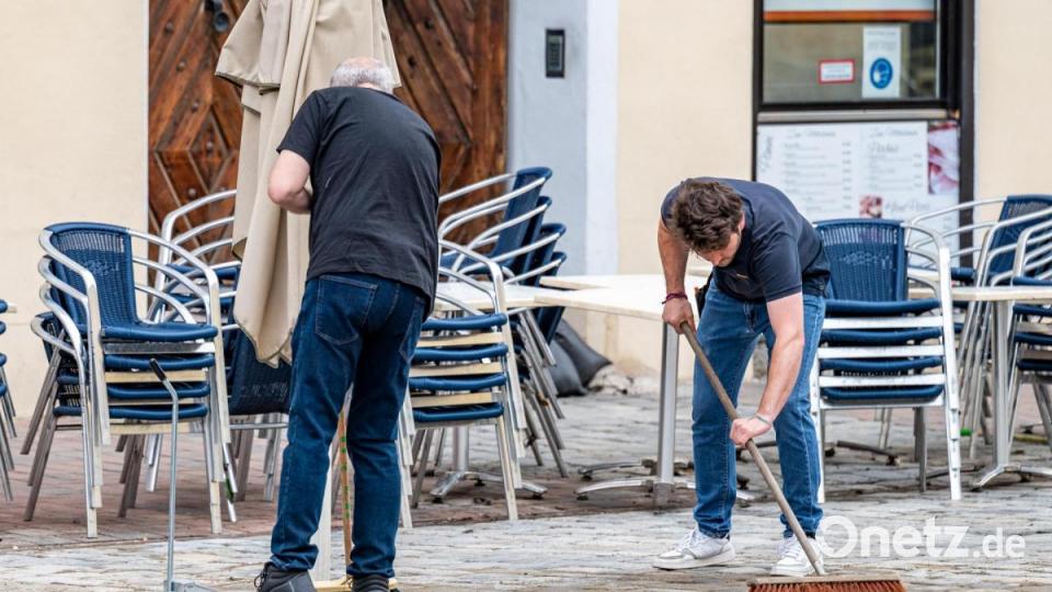 Zwei Männer kehren vor einem Café in Landshut die Überreste des Unwetters am Vorabend weg. Bild: Armin Weigel/dpa