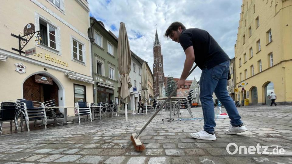 in Mann kehrt vor einem Café in Landshut die Überreste des Unwetters am Vorabend weg. Bild: Armin Weigel/dpa