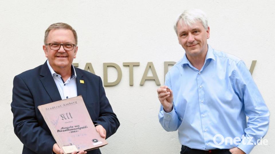 Bürgermeister Martin Preuß (links) und der Leiter des Stadtarchivs, Andreas Erb, mit der Amberger Porzellanmünze, die exakt vor 100 Jahren zum 500. Jubiläum der Martinskirche produziert worden ist, und der Akte mit den dazugehörigen Schriftstücken. Bild: Schwab Susanne, Stadt Amberg /exb