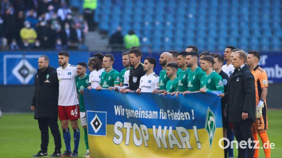 Die Spieler vom Hamburger SV und SV Werder Bremen stehen vor dem Spiel während einer Schweigeminute für die Ukraine zusammen, und halten ein Banner mit der Aufschrift "Wir gemeinsam für Frieden! stop war!" Bild: Christian Charisius/dpa