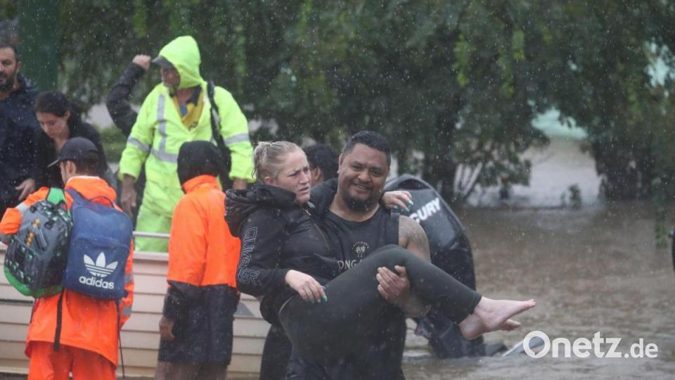 Ein Mann trägt eine Frau durch das Hochwasser einer überschwemmten Straße im australischen Lismore. Bild: Jason O‚äôbrien/AAP/dpa