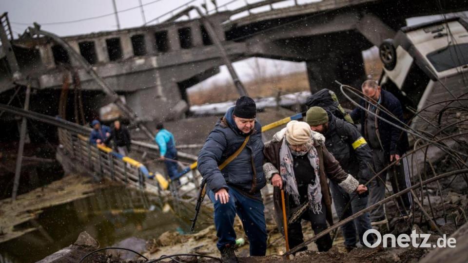 Örtliche Milizionäre helfen einer alten Frau über eine zerstörte Brücke am Stadtrand von Kiew. Bild: Emilio Morenatti/AP/dpa