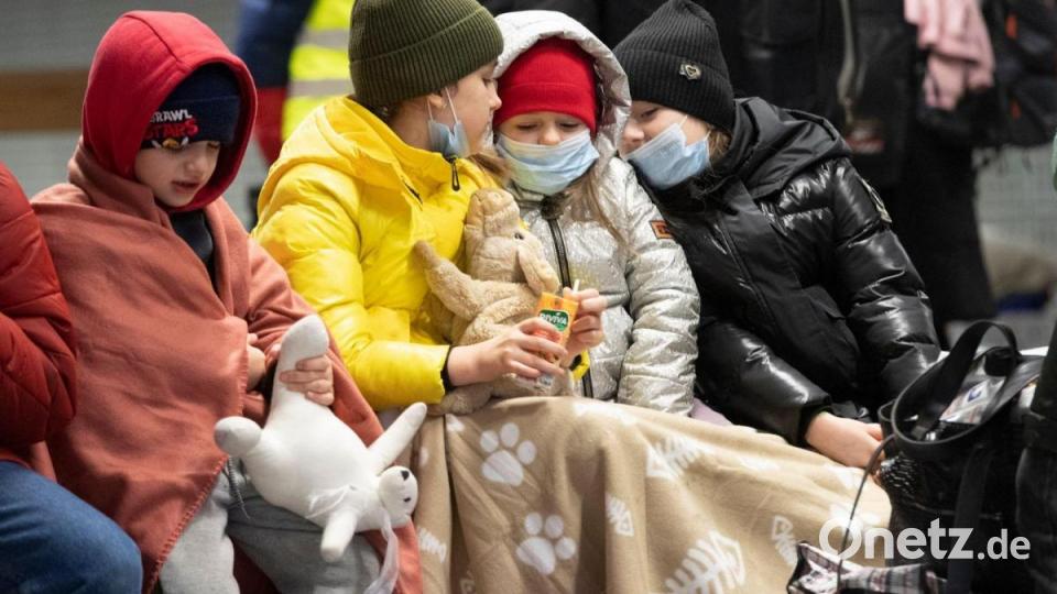 In Decken gehüllt sitzen diese Kinder aus dem ukrainischen Kriegsgebiet auf einer Bank im Berliner Hauptbahnhof. Bild: Paul Zinken/dpa