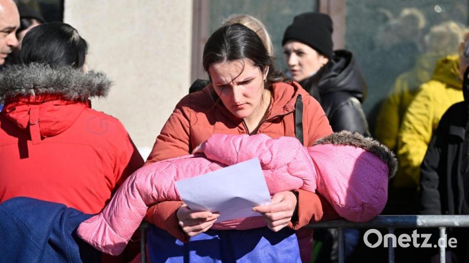 Menschen wartet mit einem Kind im Arm vor einem Zentrum zur Registrierung und Unterbringung von Geflüchteten in Brüssel. Bild: Eric Lalmand/BELGA/dpa
