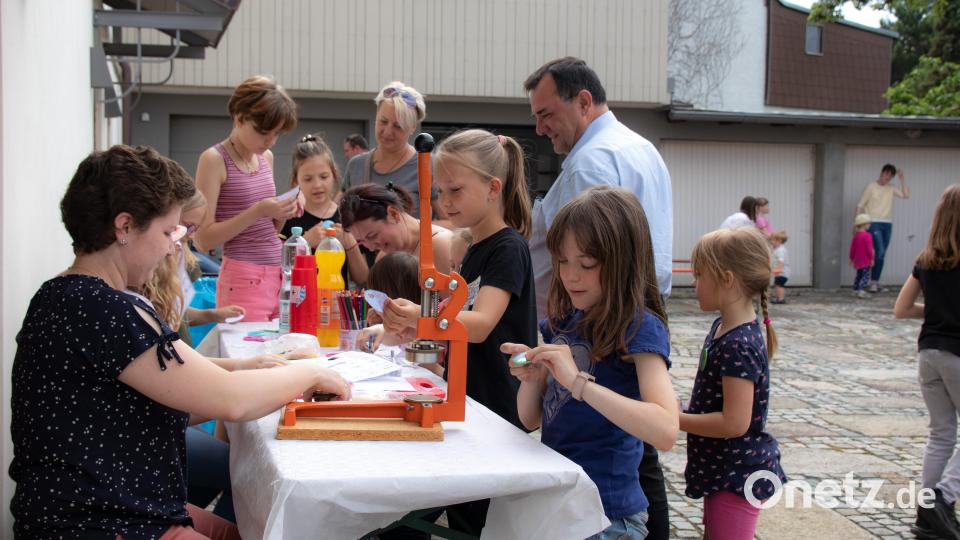Pastoralreferentin Maria Wagner (links) bastelt beim Spielenachmittag für deutsche und ukrainische Kinder im Pfarrhofgarten Anstecker mit den jungen Gästen. Pfarrer Konrad Amschl beobachtet die Aktion. Bild: sfo