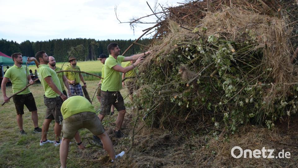 Während sich der Platz um das Johannisfeuer des „Jung’sell’n Club“ auf dem Fuchssteinach, hoch über Vohenstrauß gut füllt, sind die jungen Männer noch damit beschäftigt, die letzten Äste auf den Johannisfeuerstapel zu schichten, der bei Anbruch der Dunkelheit entfacht wurde. Ein Shuttle-Bus bringt die Gäste bequem auf die rund vier Kilometer entfernte Anhöhe und später auch wieder zurück. Der Holzstapel wurden eigens noch wenige Stunden davor umgeschichtet worden, damit sich dort kein Tier versteckt hält, dass dann qualvoll verenden würde. Die Burschen handelten beispielgebend. Bild: dob