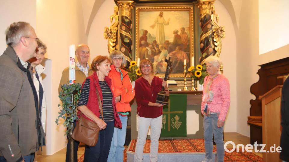 Traudl Klinger (Mitte) zeigt das mit einer Widmung des Spenders versehene Altarkreuz in der evangelischen Nikolauskirche in Etzenricht. Auf dem Altarbild im Hintergrund sollen Etzenrichter Bürger dargestellt sein. Bild: war