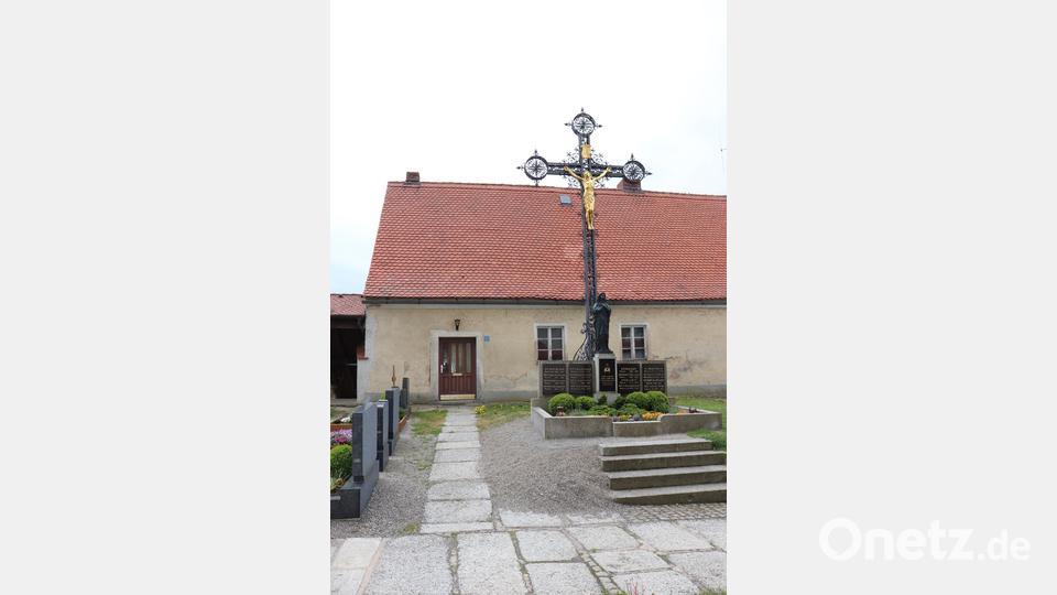 Blick vom Kircheneingang in Richtung des Kooperatorhauses mit dem Kreuz davor. Der Zugang liegt direkt am Friedhof in das historische Gebäude. Bild: flt