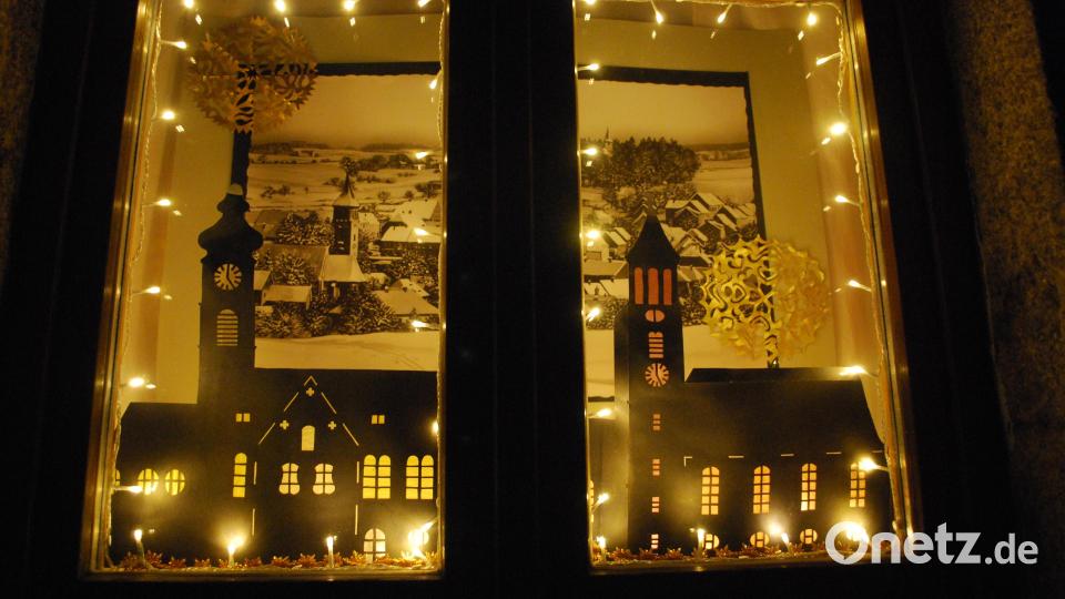 Im ehemaligen Flosser Bahnhof leuchten wieder Winterfenster. In diesem hier sind die beiden großen Kirchen als Scherenschnitte zu sehen, dahinter eine historische Ansicht vom Ort. Bild: tss