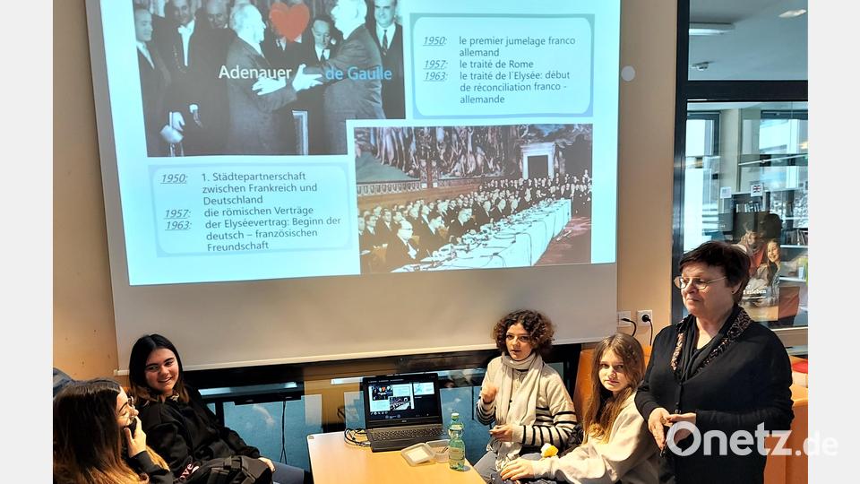 „Hier die große Politik, da die menschliche Seite an der Basis!“ Die französische Deutschlehrerin Jocelyne Gandil (rechts) zusammen mit einigen Schülerinnen vor einem Bild der Power-Point-Präsentation zum Jubiläum des Elysée-Vertrags. Bild: lg