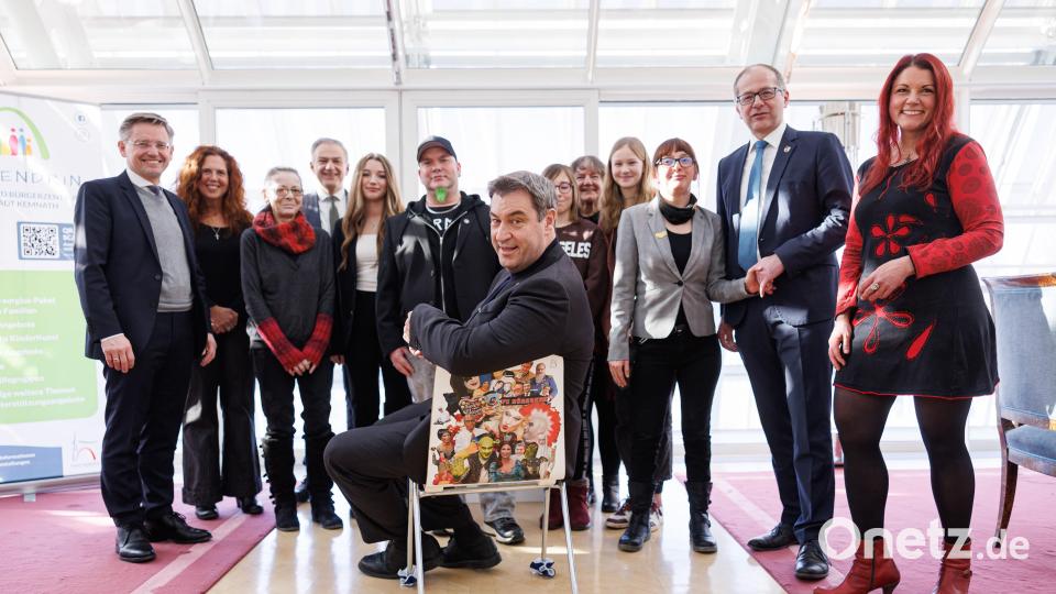 Eine Delegation des Projekts Kinder-Kunst überraschte Ministerpräsident Markus Söder mit einem ungewöhnlichen Stuhl. Natürlich musste Söder gleich probesitzen.Sehr zur Freude der Macher sowie von MdL Tobias Reiß (links), Landrat Roland Grillmeier (Vierter von links), Bürgermeister Roman Schäffler (Zweiter von rechts) und Mittendrin-Leiterin Jessika Wöhrl-Neuber (rechts) bleibt der Suhl im Büro des Ministerpräsidenten stehen. Bild: Bayerische Staatskanzlei/exb