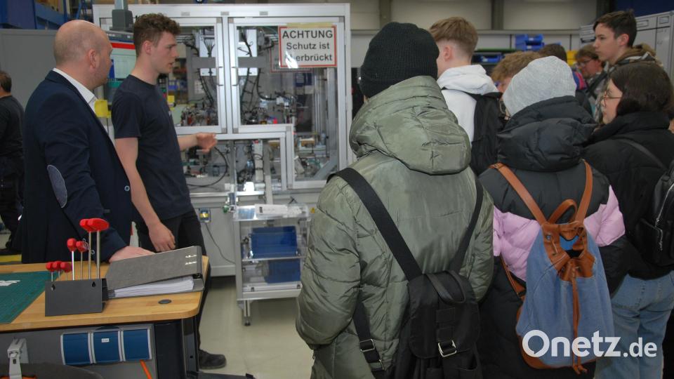 Alexander Pösl (Produktionsleiter bei PIA) und Tim Piehler (ehemaliger Azubi bei PIA) stellen einer Schülergruppe eine von Azubis entwickelte Montageanlage vor. Bild: gsp