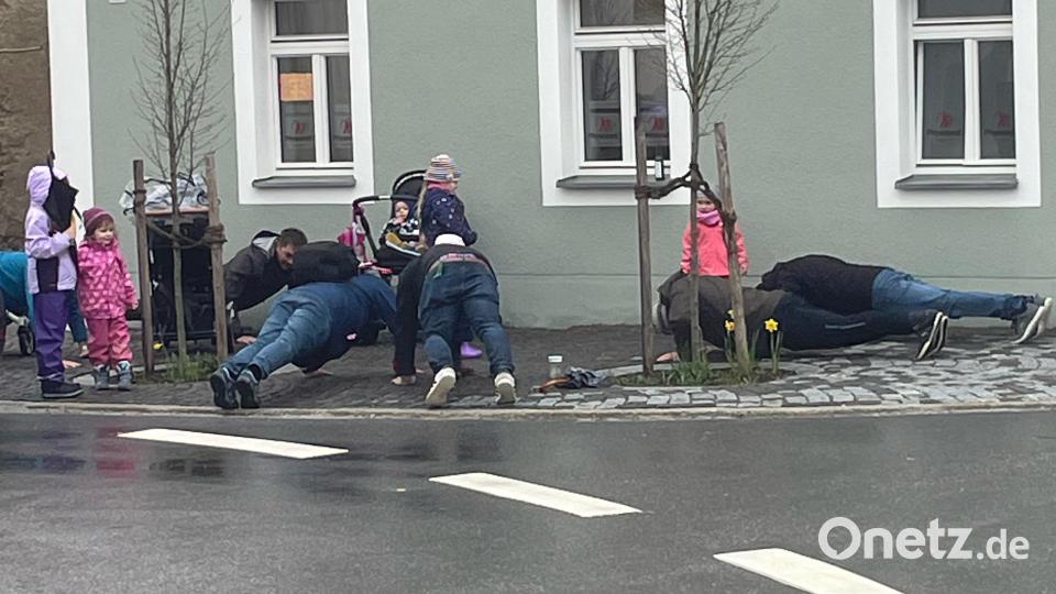 Sportliche Aufgaben - hier zehn Liegestützen - müssen die Väter bei der Vater-Kind-Rallye am Bürgersteig vor dem Physiocenter erfüllen. Bild: fvo