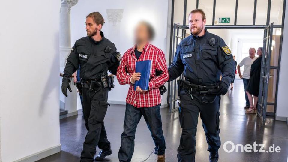 Der Angeklagte, der dreifach gefesselt ist, wird von Polizisten zum Gerichtssaal geführt. Bild: Armin Weigel