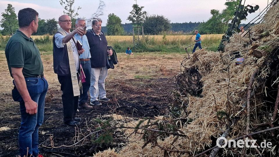 Die Brandstelle des ersten Holzhaufens ist noch zu sehen. Für das Abbrennen des &quot;Ersatzhaufens&quot; zur Sommersonnenwende gibt es von Ruhestandspfarrer Andreas Uschold im Beisein von Hans Sperrer (von rechts) und Alois Lukas vom OWV den Weihwassersegen. Diesmal klappte alles. Bild: R. Kreuzer