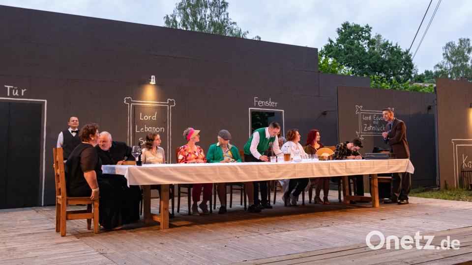 An einer langen Tafel verliest Anwalt Frank Tanner (Oswald Hamann, rechts) das Testament von Lord Lebanon. Sie ist der Hauptschauplatz des Theaterstücks. Bild: Susanne Forster