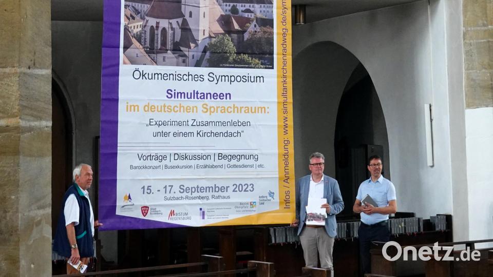 Stadtpfarrer Herbert Mader (oben links) und Stadtpfarrer Roland Kurz (oben rechts) entrollen das Banner, das am Gerüst der Baustelle St. Marien aufgehängt wird und auf das Symposium hinweist. Bild: gac