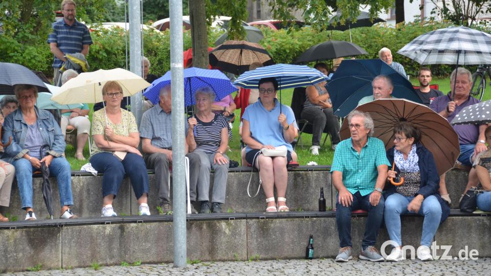 Die Zuhörer spannen ihre Regenschirme auf und bleiben beharrlich sitzen, um der Blasmusik zu lauschen. Bild: dob