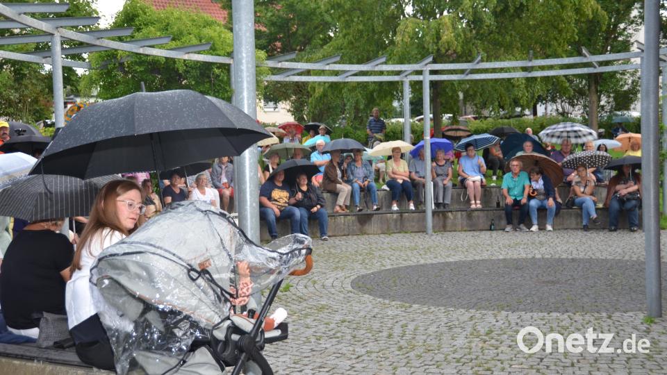 Die Zuhörer spannen ihre Regenschirme auf und bleiben beharrlich sitzen, um der Blasmusik zu lauschen. Bild: dob