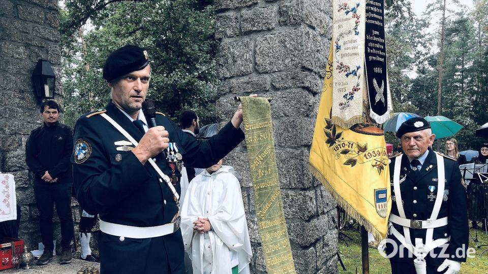 Für seine Ansprache hatte Wolfgang Danler (links), Vorsitzender der Krieger-, Soldaten- und Reservistenkameradschaft Mitterteich, ein 100 Jahre altes Fahnenband als Anschauungsstück mitgebracht. Bild: wro