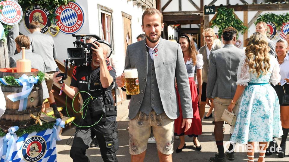 Der Spieler des FC Bayern, Harry Kane steht mit einer Maß Bier und in kurzen Lederhosen vor dem Käferzelt. Bild: Felix Hörhager