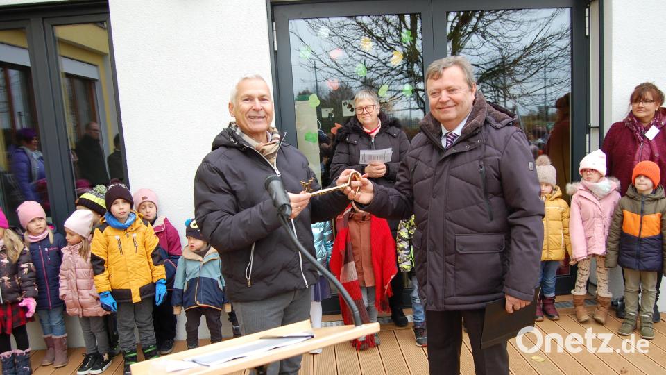 Architekt Olaf Götzer (links) überreichte den symbolischen Schlüssel für die Kindergartenerweiterung an Bürgermeister Gerhard Keller (rechts), der diesen an dann an Kindergartenleiterin Emmi Garg (hinten, Mitte) weiterreichte. Die Kindergartenkinder umrahmten mit Tanz und Gesang die Einweihungsfeier. Bild: sm