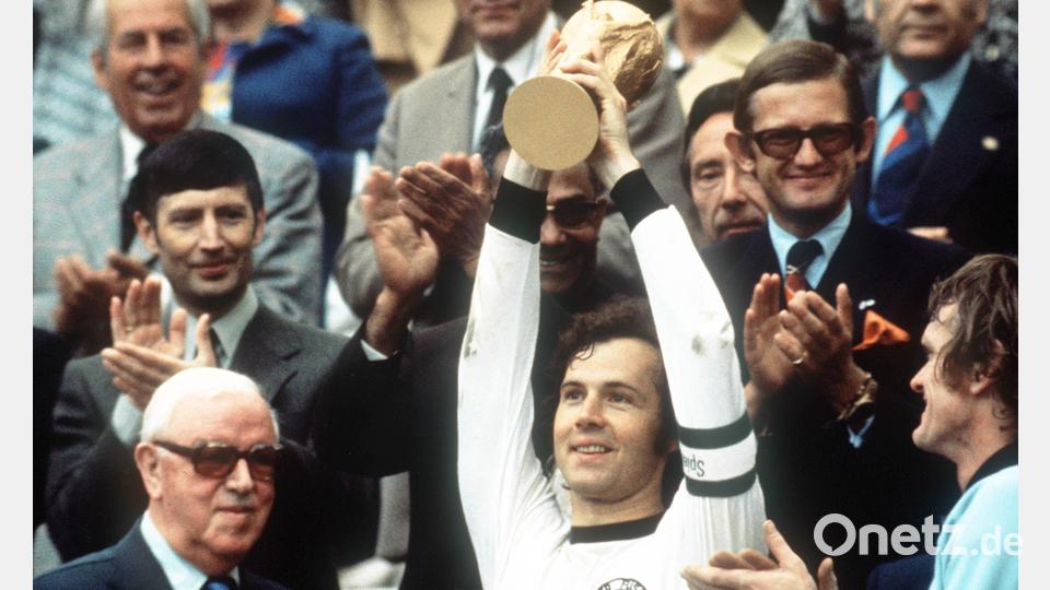 Franz Beckenbauer (M) hebt an der Seite von Torhüter Sepp Maier (r) und dem englischen FIFA-Präsidenten Stanley Rous (l) am 07.07.1974 im Münchner Olympiastadion nach dem Endspiel der Fußball-WM den eroberten WM-Pokal triumphierend hoch. Die deutsche Fußballnationalmannschaft gewann das Finale der Fußball-Weltmeisterschaft gegen die Niederlande mit 2:1. Bild: Hartmut Reeh/dpa