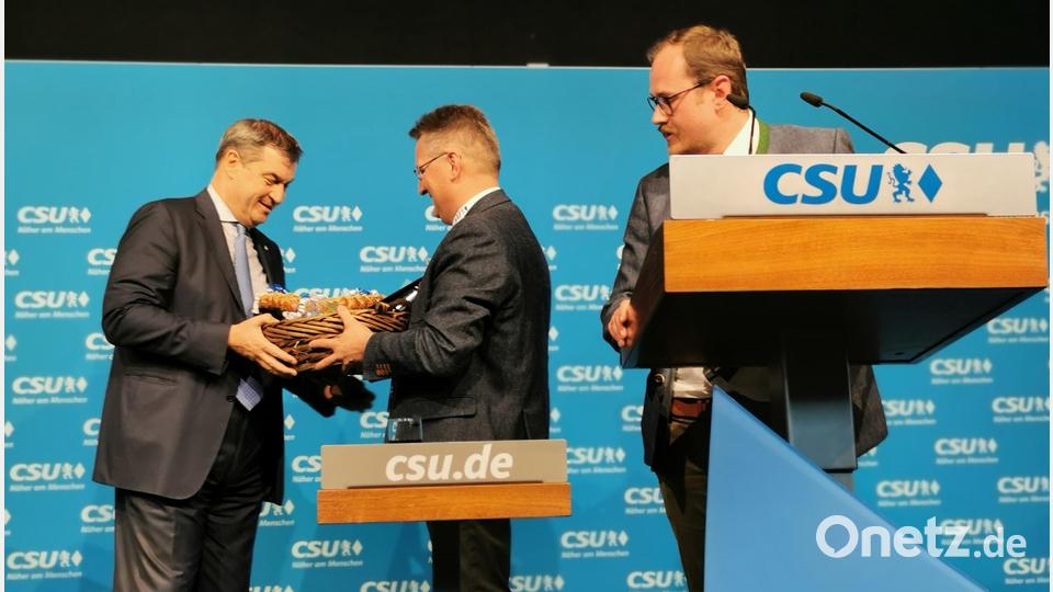 Der Oberviechtacher CSU-Ortsvorsitzende Tobias Ehrenfried (rechts) bedankt sich mit einer launigen Ansprache bei Markus Söder, während der Teunzer CSU-Ortsvorsitzende Adolf Hammer einen Korb mit regionalen Produkten überreicht. Bild: Portner