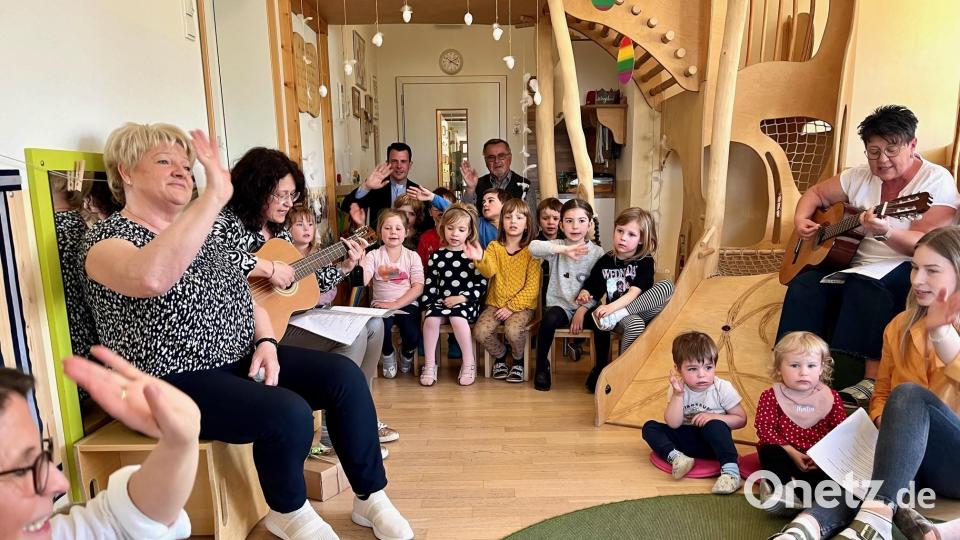 Einen letzten Gruß senden die Kinder der Kita St. Dionysius an die langjährige Krippenpädagogin Elke Forster. Die 62-Jährige (links im Bild neben Kita-Leiterin Lydia Hofmann an der Gitarre) winkt zurück. Im Hintergrund sind Pfarrer Thomas Kohlhepp sowie Willibald Fuchs von der Kirchenverwaltung zu sehen. Bild: Gabi Schönberger
