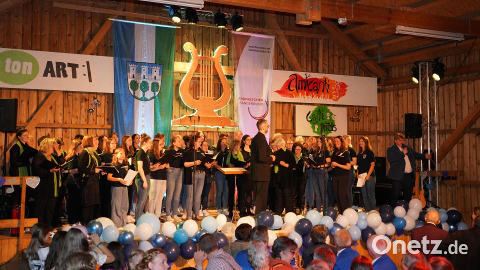 Die Chöre &quot;tonART&quot; und &quot;amicanti&quot; sowie Moderator Hans-Peter Reil (rechts) auf der Bühne beim Jubiläumskonzert des Gesang- und Orchesterverein Waldthurn in der Vereinshalle. Bild: fvo