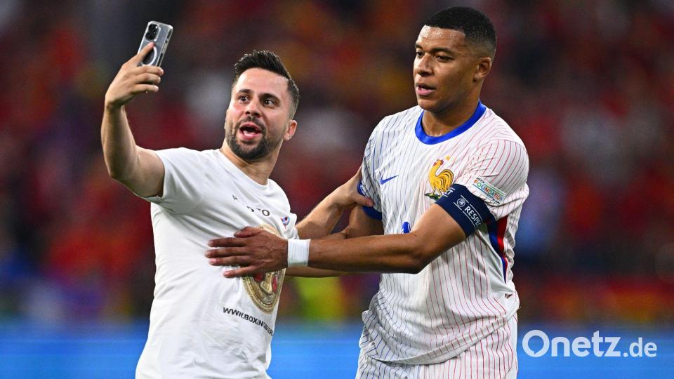 Ein „Flitzer“ ist aufs Spielfeld gelaufen und macht ein Selfie mit Frankreichs Kylian Mbappe (r). Bild: Tom Weller/dpa