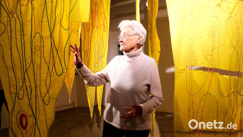 Künstlerin Beate Oehmann inmitten einer raumgreifenden Installation, bei der sie Stoff aus gelben Fahnen bearbeitet hat - ein Sonne aus Stoff und genähten Spuren. Bild: Peter Ringeisen