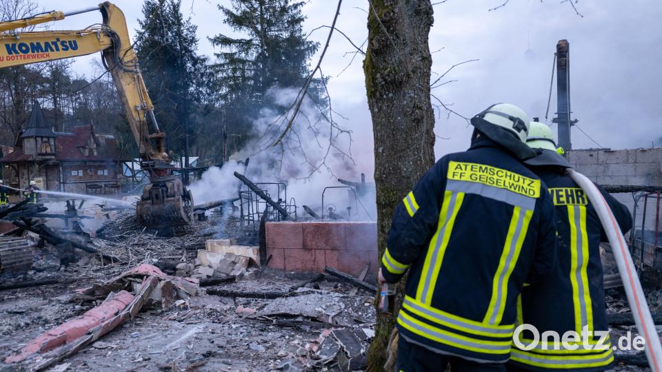 Ein Bagger hebt Holz-, Metall- und Gebäudeteile von einem Brandort, daneben besprechen sich zwei Einsatzkräfte der Feuerwehr. Im Freizeit-Land Geiselwind ist ein Feuer ausgebrochen. Ein Kiosk und der Gaststättenbereich im Eingang des Freizeitparks sind vollständig zerstört. Bild: Pia Bayer