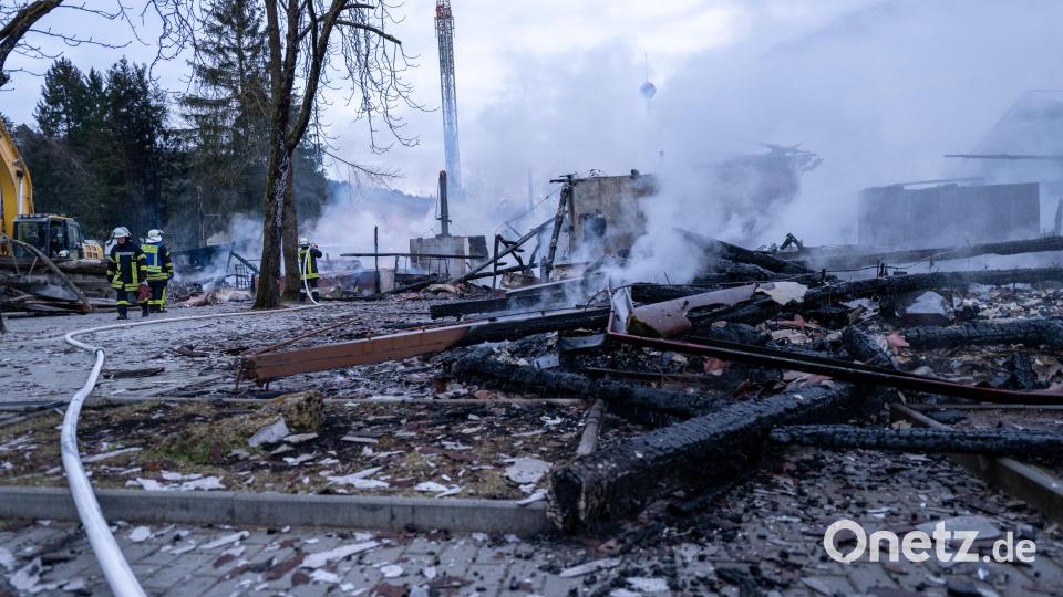 Verkohlte Holzbalken liegen am Boden und Rauch steigt auf, während im Hintergrund der Turm einer Attraktion im Freizeit-Land Geiselwind zu erkennen ist. Im Freizeit-Land Geiselwind ist ein Feuer ausgebrochen. Bild: Pia Bayer
