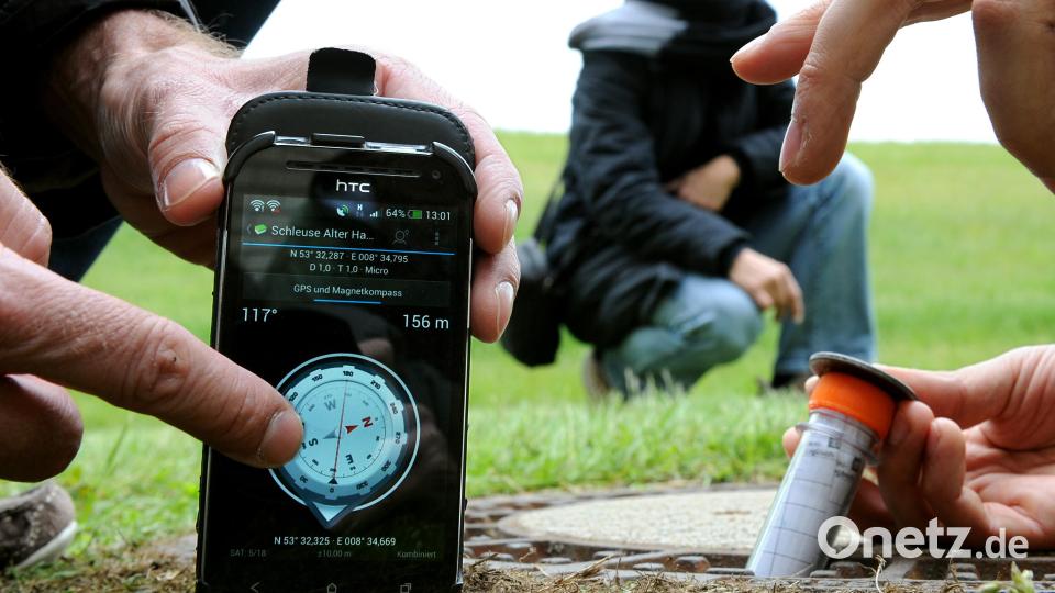 Geocacher haben mithilfe eines GPS-Geräts ein in einer Röhre verpacktes Mini-Logbuch in einem Kanaldeckel gefunden. Symbolbild: Ingo Wagner/dpa
