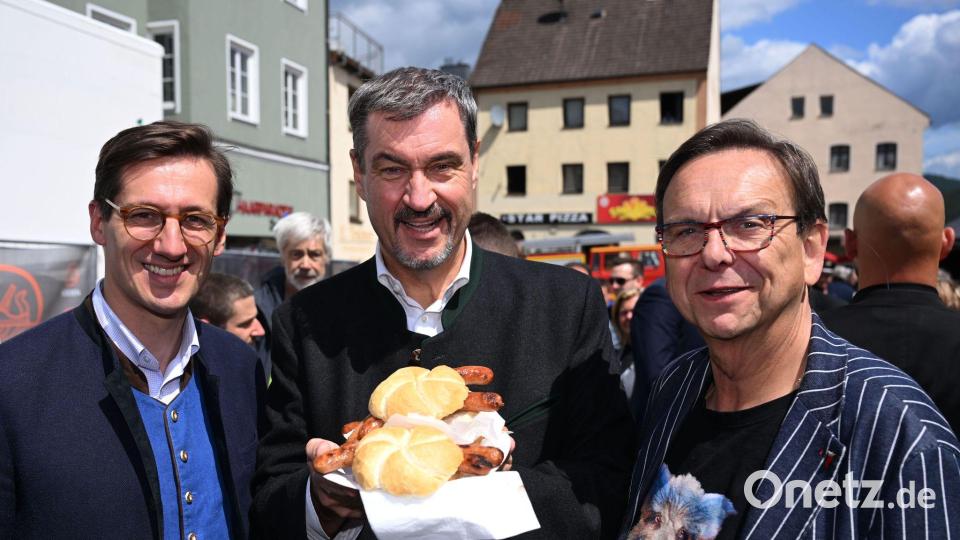 Markus Söder (M.) hält Bratwurst-Semmeln in die Kamera. Bild: Felix Hörhager/dpa