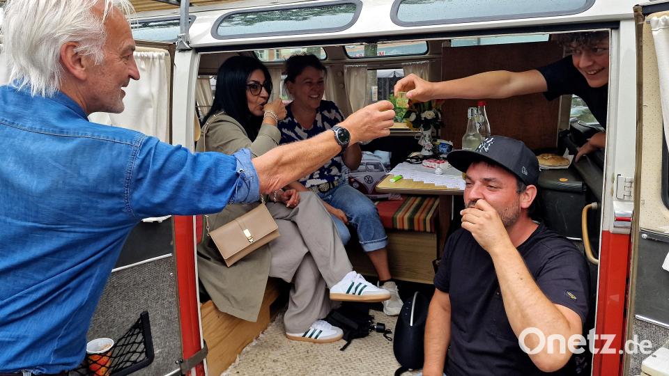 Gerhard Wölfls VW-Bus als rollende Campinglounge – Wölfl (links) gibt schon mal einen Likör an die Betrachter aus. Bild: R. Kreuzer