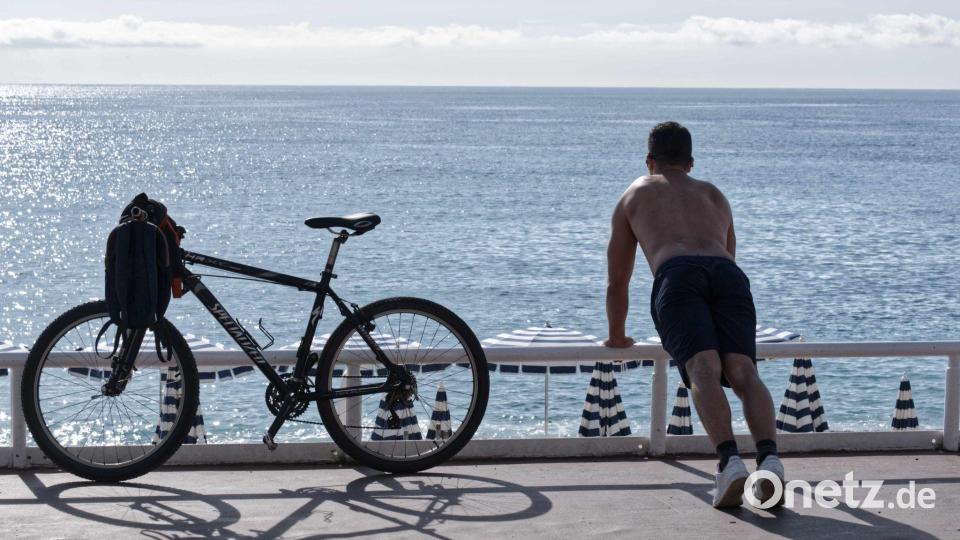Ein Mann mit nacktem Oberkörper macht am Strand von Nizza neben seinem Fahrrad Übungen. (Archivbild) Bild: Serge Haouzi/XinHua/dpa