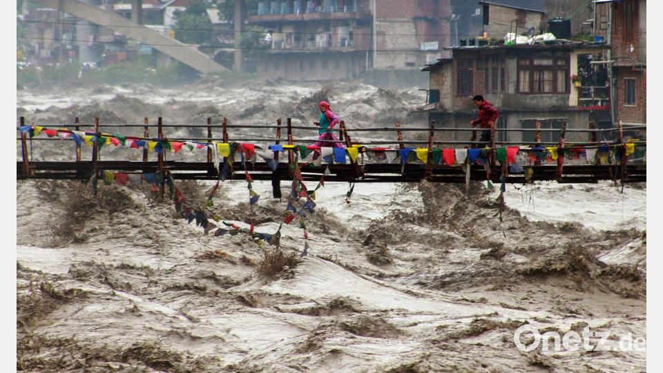 Menschen wagen im nordindischen Bundesstaat Himachal Pradesh trotz schwerer Überschwemmungen den Weg über eine Brücke, um den Fluss Beas zu überqueren. Bild: Aqil Khan/AP/dpa