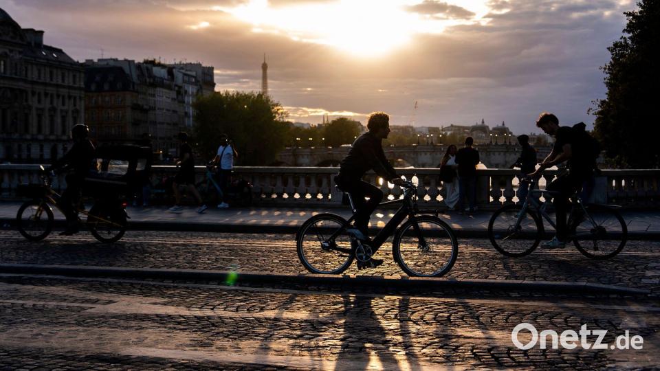 Menschen fahren bei Sonnenuntergang mit dem Fahrrad auf einer Brücke über die Seine in Paris. Bild: Julia Demaree Nikhinson/AP/dpa