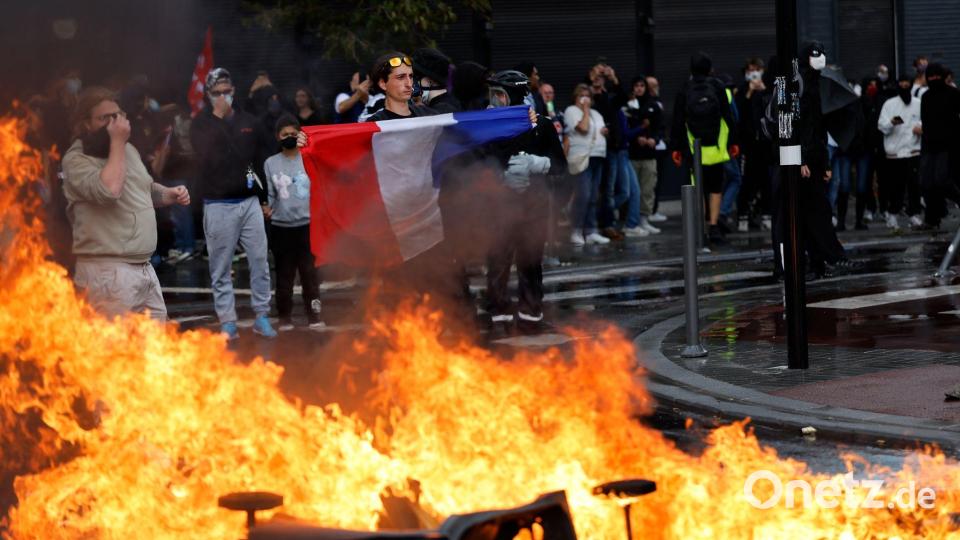 Ein Demonstrant der Protestbewegung „Bloquons Tout“ (Alles blockieren) zeigt eine französische Nationalflagge neben brennenden Mülltonnen. Bild: Jean-Francois Badias/AP/dpa