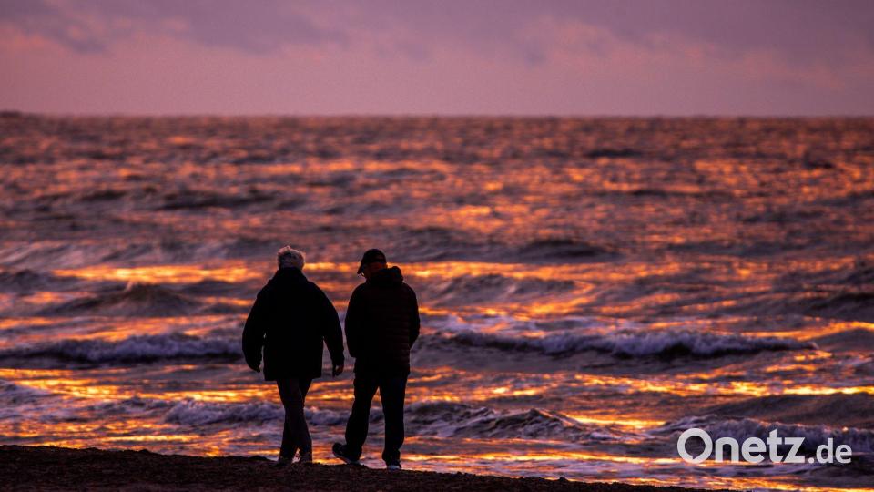 Spaziergänger sind nach Sonnenuntergang am Strand von Warnemünde an der Ostsee unterwegs. Bild: Jens Büttner/dpa