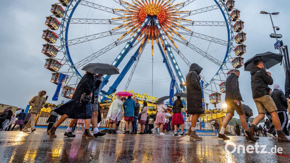 Besucher des Oktoberfestes in München gehen im Regen über das Festgelände vor dem Riesenrad. Bild: Armin Weigel/dpa