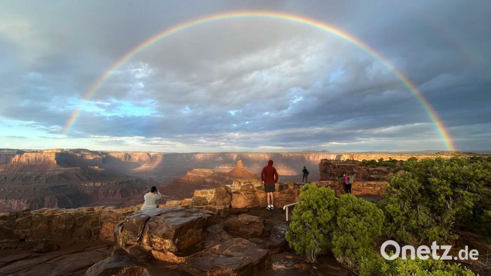 Menschen stehen an einem Aussichtspunkt, während ein doppelter Regenbogen am Himmel über dem Dead Horse Point State Park in der Nähe von Moab in den USA leuchtet. Bild: Becky Bohrer/AP/dpa