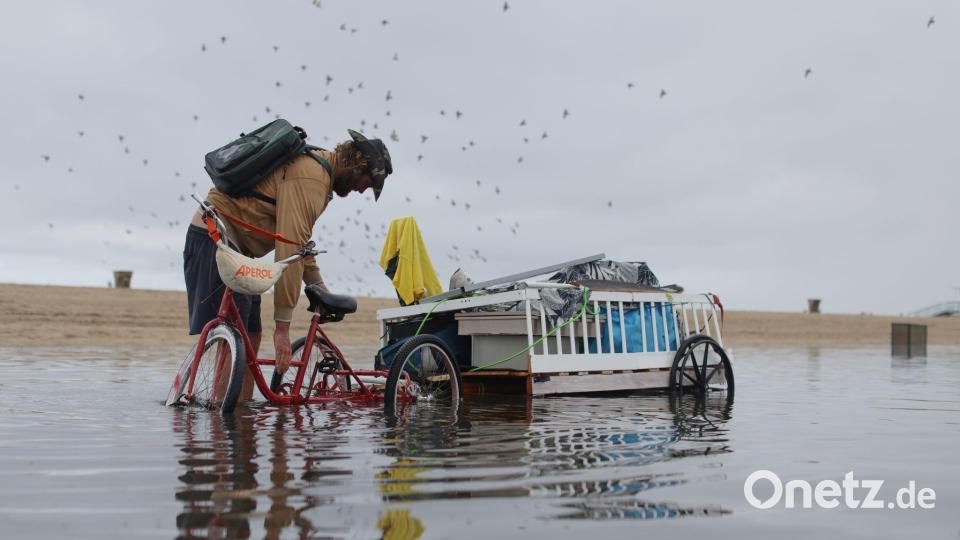 Ein Mann passt seine Ladung auf dem Fahrradanhänger an, um den durch heftigen Regenfällen überfluteten Weg entlang zufahren. Bild: Ethan Swope/FR171736 AP/dpa