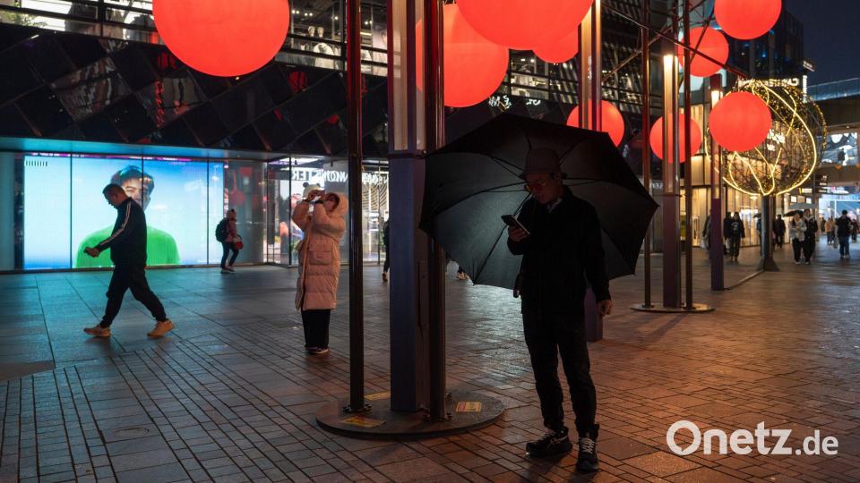 Ein Mann schaut auf sein Telefon in der Nähe von roten Zierkugeln am Taikoo Li Sanlitun Einkaufszentrum in Peking. Bild: Ng Han Guan/AP/dpa