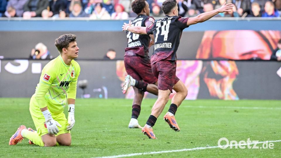 Augsburgs Torwart Finn Dahmen kauert bedröppelt am Boden, die Leipziger Assan Quedraogo (M) und Christoph Baumgartner (r) bejubeln das 0:5. Bild: Harry Langer/dpa