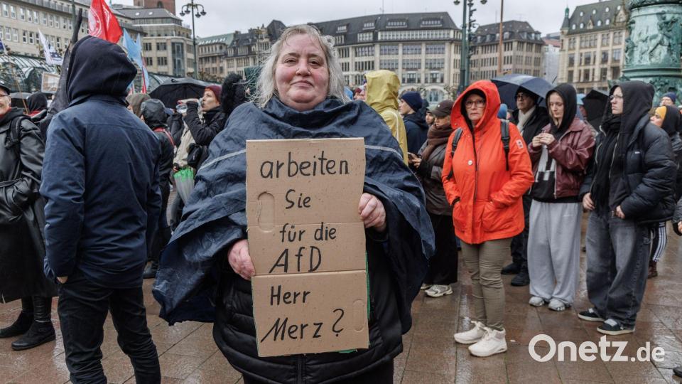 Eine Demonstrantin in Hamburg stellt auf einem Pappschild eine Frage an Bundeskanzler Friedrich Merz (CDU). Bild: Markus Scholz/dpa
