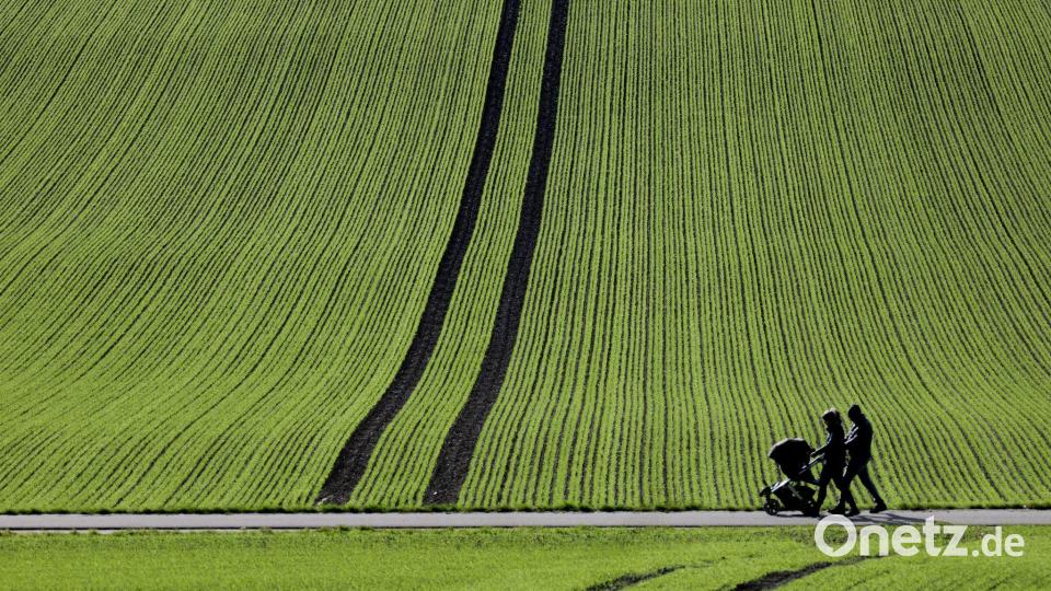 Spaziergänger gehen im Sonnenschein an einem frisch bestellten Feld in Baden-Württemberg vorbei. Bild: Thomas Warnack/dpa