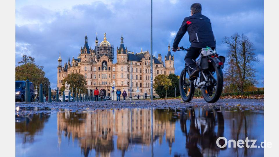Herbstwetter in Norddeutschland: Ein Radfahrer fährt an einer Pfütze vorbei, in der sich das Schweriner Schloss spiegelt. Bild: Jens Büttner/dpa